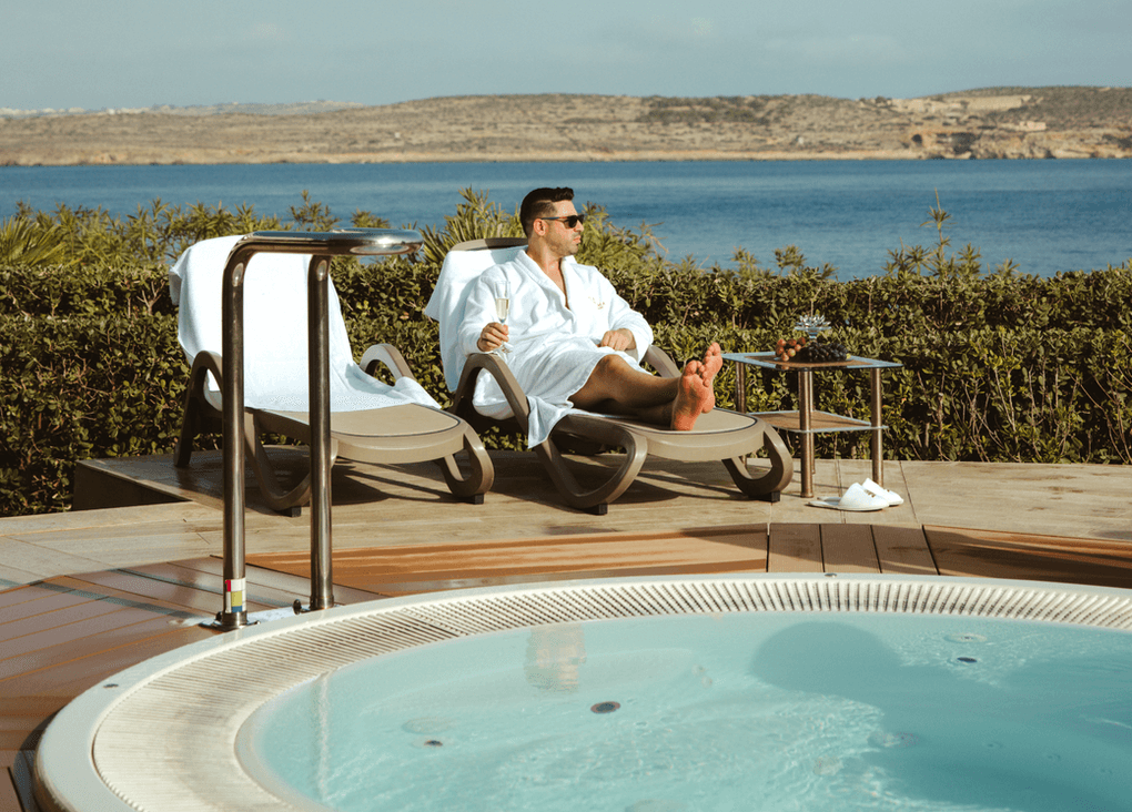Man relaxing on a sun lounger beside the outdoor spa pool, overlooking the sea